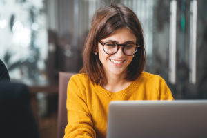 Porträt einer glücklichen Geschäftsfrau mit Brille am Arbeitsplatz im Büro. Junge hübsche Arbeitnehmerin mit modernem Laptop